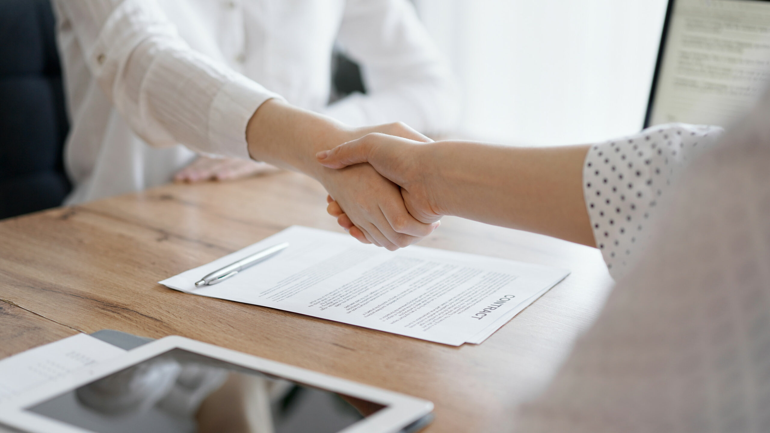 Business people shaking hands above contract papers just signed on the wooden table, close up. Lawyers at meeting. Teamwork, partnership, success concept